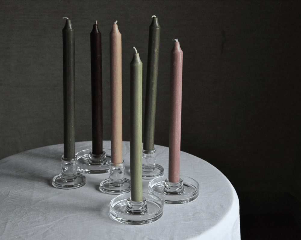 Sex runda ljusstakar i glas med kronljus i färgerna grön, brun och rosa.